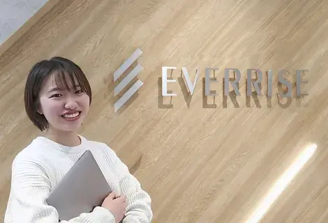 EVERRISEロゴ前で笑顔のエンジニア社員