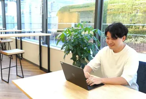 若手社員が開放的なオフィスで楽しそうにPC作業をしている様子